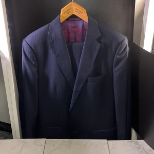 Marinblå kavaj och byxor från Senziu  - Elegant blå kavaj och matchande byxor från Senziu, tillverkad av Vitale Barberis Canonico-tyg. Kavajen har ett stilrent mönster och en färgglad foder med röda detaljer. Perfekt för formella tillfällen och skapar dig till den mest välklädda på plats. Hör av er vid minsta fundering🙌