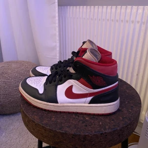 Nike Air Jordans i svart, vitt och rött - Snygga Nike Air Jordans i klassisk färgkombination av svart, vitt och rött. Skorna har en hög modell med snörning och den ikoniska swoosh-loggan i rött på sidan. Perfekta sneakers!