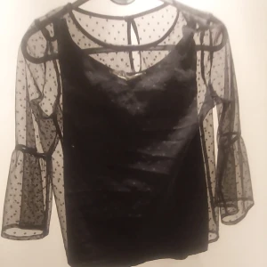 Här är en svart prickig tröja från H&M - Svart prickig tröja som är genomskinlig vid armarna. Tröjan har en inbyggd svart linne. 