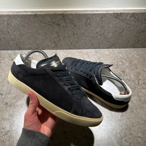 Saint Laurent skor - Snygga svarta sneakers i mocka från Saint Laurent. Dom är i bra skick. Dom passar 42 i skostorlek. Nypris ligger på runt 7299kr och här kan du köpa dom för bara 2099kr. Vid fler frågor är det bara att skriva. Box saknas. 