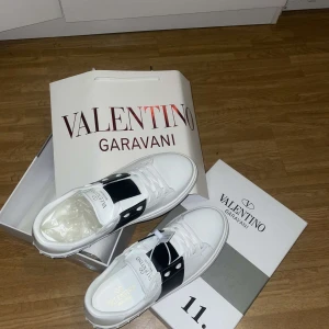 Valentino Garavani sneakers i vitt och svart - Snygga Valentino Garavani sneakers i vitt med svarta detaljer. Skorna har snörning och en stilren design som passar perfekt för en trendig look.