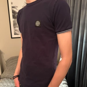 Mörkblå t-shirt från Stone Island - Mörkblå Tee från STONE ISLAND med vita detaljer på ärmarna. Storlek junior men passar S, stor i storlek. Även snygg detalj på bröstet. 