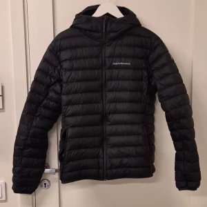 Peak Performance jacka - Säljer en stilren svart dunjacka från Peak Performance. Jackan har en praktisk huva och dragkedja framtill. Skicket är 7/10 och det finns tecken på användning vid ärmarna. Priset går att distukteras.