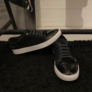 Lanvin skor  - Snygga svarta sneakers med glansig yta och vita sulor. Skorna har snörning och en stilren design som passar perfekt till vardagsbruk.  De är slitna i sulan men får med får med en whitening cream för sulorna. Skick 8 av 10.  Endast skorna följer med. Priset är ej hugget i sten