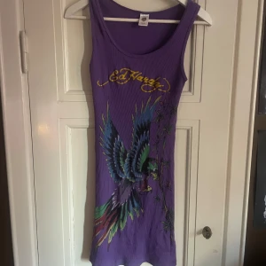 Lila klänning från Ed Hardy - Snygg lila klänning från Ed Hardy med ett stort färgglatt fågeltryck på framsidan stor logga på fram och baksida. Klänningen är ärmlös och har en tight passform, perfekt för en cool och avslappnad stil. Stretchig! Passar xs-M