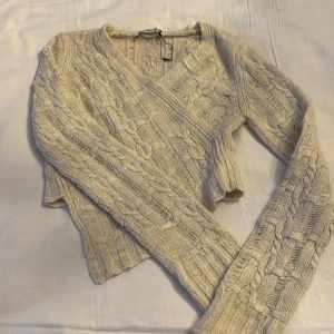 Beige stickad tröja från Zara - Säljer en snygg beige stickad tröja från Zara med ett flätat mönster. Tröjan har en v-ringad design och långa ärmar, perfekt för kyligare dagar. Den är både stilren och bekväm.