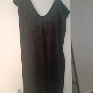 Svart långklänning med blommigt mönster - Säljer en elegant svart sammetsklänning med ett subtilt blommigt mönster. Klänningen har en v-ringad design och är ärmlös, vilket gör den perfekt för festliga tillfällen. Perfekt föe julfesten! Egensydd.