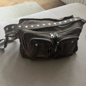 Nunoo väska  - I fint skick, finns ett längre regelbart band till också så man kan justera den för den längden man vill ha.  Bredd: 24 Höjd: 16 Djup: 9 cm
