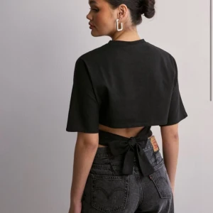 Svart croppad topp med knyt - Snygg svart croppad topp med korta ärmar och knytning i ryggen. Perfekt för en avslappnad men stilren look. Passar bra till både jeans och kjol.