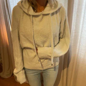 Mysig vit hoodie - Säljer en supermysig vit hoodie som är perfekt för kyliga dagar. Den är gjord i ett mjukt material och har en stor huva med långa snören. Tröjan har långa ärmar och ribbade muddar vid ärmslut och nederkant.! stickad hoodie