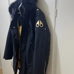 Moose knuckles stag lake parka svart - Moose Knuckles Stag Lake Parka i svart är en robust och stilren vinterjacka. Denna parka är känd för sin höga kvalitet och värmeisolering, vilket gör den idealisk för kalla vintrar. Den har en avtagbar pälskrage på huven och flera fickor för praktisk