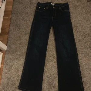 Mörkblå jeans - Säljer ett par snygga mörkblå jeans med klassisk design. De har en rak passform och är perfekta för både vardag och fest. Jeansen har gula sömmar som ger en cool kontrast och de är i bra skick.