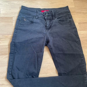 Svarta jeans med knappdetalj - Säljer ett par svarta jeans i bra skick. De har en snygg knappdetalj fram och klassiska femficksdesign. Perfekta för både vardag och fest!