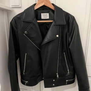 Svart skinnjacka från Zara - Säljer en snygg svart skinnjacka från Zara. Den är knappt använd och har inga defekter. Storleken har 164 men är som en Xs. Jag har storlek Xs och den sitter jätte bra! Kan gå ner i pris