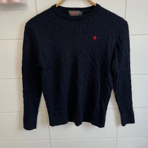 Marinblå kabelstickad tröja från Morris. - Säljer en snygg marinblå kabelstickad tröja från Morris i 100% merinoull. Den har en röd broderad detalj på bröstet och är perfekt för både höst och vinter. Det står att den är xl men sitter som ungefär xs-s på grund av att den har blivit tvättad fel av förra ägaren och blivit för liten. Frågor och funderingar? Hör bara av dig