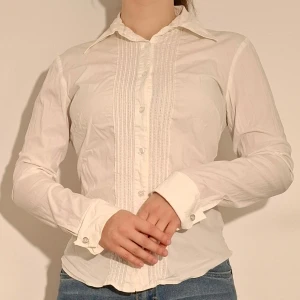 Vit skjorta - Vit skjorta med sptesdetalj längs med knapparna.  (Sista bilden visar tröjans material)