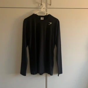 Svart långärmad tröja från Gymshark - Säljer en svart långärmad tröja från Gymshark i storlek S. Perfekt för träning eller vardagsbruk. Tröjan är i bra skick och har en stilren design med Gymshark-loggan på bröstet. Passar perfekt för höst och vår!