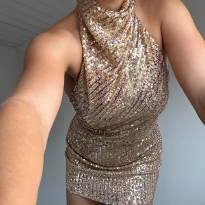 Miniklänning med halterneck och guldpaljetter  - Perfekta nyårsklänningen. Halterneck som knäpps bakom nacken med tre spännen, även gömd dragkedja vid rumpan. Aldrig använt, köpt för kanske tre år sedan 