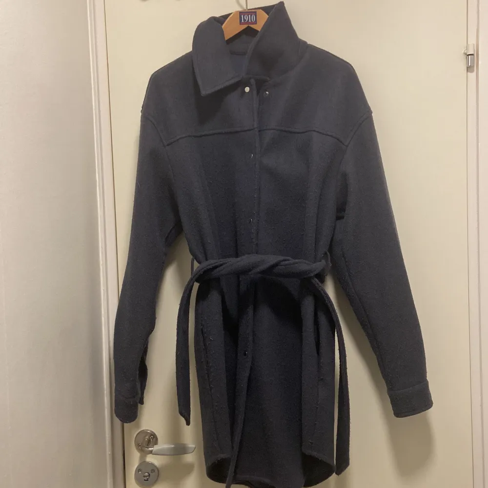 Snygg mörkblå kappa från Vero Moda med knappar och ett bälte i midjan. Perfekt för kyligare dagar med sin långa design och långa ärmar. . Takit.