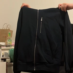 Svart jacka från Sail Racing - Snygg svart jacka från Sail Racing med dragkedja framtill och en praktisk bröstficka med dragkedja. Perfekt för en stilren look. Jackan har långa ärmar och är tillverkad i ett bekvämt material.