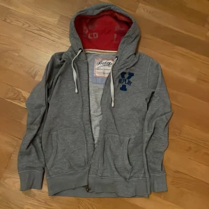 Grå zip hoodie från Replay - Säljer en grå hoodie från Replay med dragkedja och justerbar huva. Den har en blå Replay-logga på bröstet och en röd insida i huvan. Perfekt för en avslappnad stil. Bra skick men syns att den är använd, han på bilden är 181cm, kontakta vid frågor💯💯