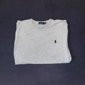 Grå Polo Ralph T-shirt - Säljer en stilren grå t-shirt från Polo Ralph Lauren med det klassiska broderade logotypen på bröstet. T-shirten är kortärmad och tillverkad i mjuk bomull för en bekväm passform. Har även använt den få gånger!