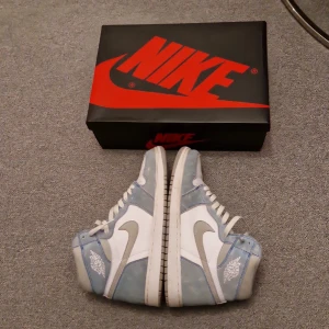 Retro High OG Hyper Royal - Snygga Nike Air Jordans i en fräsch kombination av blått och vitt. Skorna har en klassisk hög design med snörning och den ikoniska Air Jordan-loggan på sidan. Perfekta för dig som vill ha en stilren och sportig look.