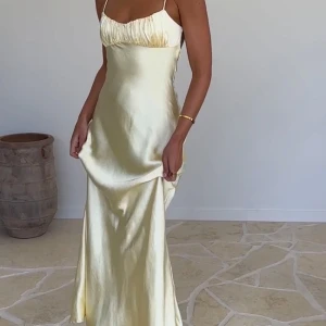 Gul maxiklänning med öppen rygg - Elegant gul långklänning i satin-imitation med smala axelband och en vacker öppen rygg. Klänningen har en lätt rynkad detalj vid bysten. Perfekt för flera tillfällen: midsommar, sommar, bal, bankett eller bröllop! Den är helt oanvänd och har kvar prislappen. Säljer för att temat för tillfället den skulle användas har ändrats!💛True to size! 