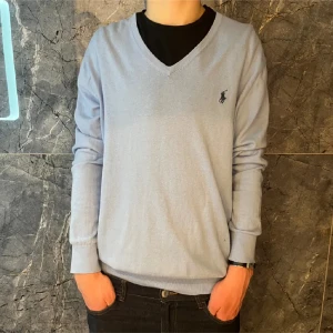 Ljusblå Kashmir tröja från Ralph Lauren - Säljer en stilren ljusblå tröja från Ralph Lauren med v-ringning och broderad logga på bröstet. Tröjan har långa ärmar och är perfekt för en avslappnad men snygg look. Storleken är L men sitter som en M, modellen är 180 cm lång