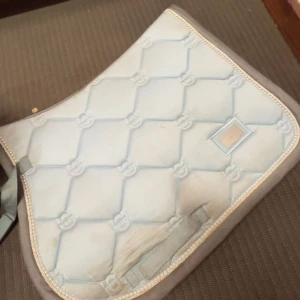 Ljusblå quiltad sadelpad från Equestrian Stockholm - Säljer en ljusblå quiltad sadelpad från Equestrian Stockholm. Den har ett elegant mönster och en diskret logotyp i silver. Perfekt för ridning och ger en stilren look till din utrustning. De kostar 600kr när det är nytt.