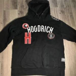 Säljer en svart hoodie från Hoodrich med flera coola patches och broderade detaljer. Den har en stor ficka framtill och justerbar huva. Perfekt för en avslappnad stil.