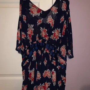 Blommig klänning från JustFab - Säljer en vacker blommig klänning från JustFab i storlek 3X. Klänningen har ett mörkblått tyg med röda och vita blommor, vilket ger en romantisk känsla. Den har en lös passform och korta ärmar, perfekt för en somrig look. Skulle säga att den passar mellan L-3XL. 