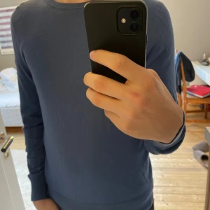 Blå tröja från Tiger of Sweden - Säljer en stilren blå tröja från Tiger of Sweden. Tröjan har en klassisk rund hals och långa ärmar, perfekt för en avslappnad men ändå elegant look. Passar bra till både jeans och chinos. Jag är osäker om storleken är S eller M men den passar precis på mig som är 178 cm lång. 