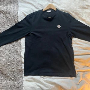 Svart långärmad tröja från Moncler - Säljer en stilren svart långärmad tröja från Moncler. Tröjan har en rund halsringning och Monclers logotyp på bröstet. Perfekt för en avslappnad och snygg look. Ny pris 4999 och är använd 5 gånger.