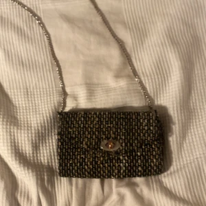  axelväska från Beck Söndergaard (pris kan diskuteras) - Snygg axelväska från Beck Söndergaard med ett unikt mönster i svart och beige. Väskan har en silvrig kedjerem och ett elegant spänne framtill. Perfekt för att ge din outfit en stilfull touch. Små slitningar vid öppning men ingenting man tänker på, därav pris (se sista bilden)