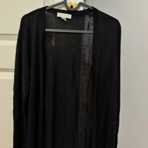 Svart kofta från H&M - Säljer en stilren svart kofta från H&M. Den är långärmad och har en enkel design som passar perfekt för lager-på-lager. Perfekt för både vardag och mer uppklädda tillfällen.