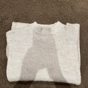 Grå stickad tröja från 157 - Mysig grå stickad tröja från 157 i storlek XS. Perfekt för kyliga dagar med sin mjuka och varma känsla. Tröjan har en klassisk design med långa ärmar och ribbade kanter vid hals, ärmslut och nederkant.