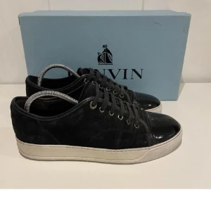  Lanvin 41-42 Uk7 - Snygga svarta sneakers från Lanvin med en kombination av mocka och lackdetaljer på tån. Skorna har en klassisk snörning och en vit sula som ger en stilren kontrast. Sko snören slitna. Box ingår! Kan gå ner i pris vid snabb affär! Fraktar samma dag. 