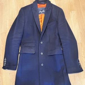Mörkblå kavaj från Zara Man - Snygg mörkblå kavaj från Zara Man med klassisk design och orange foder. Kavajen har knappar framtill och vid ärmsluten samt fickor med lock. Perfekt för en stilren look. Nypris: 2500 kr.