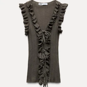 Trendiga volangtopp från Zara - Snygg grön ribbad topp från Zara med volangdetaljer längs den djupa v-ringningen. Toppen är ärmlös och har knytband framtill för en extra touch. Perfekt för att piffa upp garderoben!