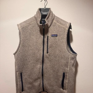 Beige fleeceväst från Patagonia - Säljer en beige fleeceväst från Patagonia med dragkedja och två fickor framtill. Västen har en stilren design och är perfekt för lager-på-lager under kyligare dagar. 