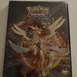 Pokémon Trading Card Game pärm - Säljer en Pokémon Trading Card Game pärm med ett motiv av en gyllene Pokémon på framsidan. Pärmen har plastfickor för att förvara och organisera samlarkort. Perfekt för Pokémon-entusiaster som vill hålla sina kort i gott skick.