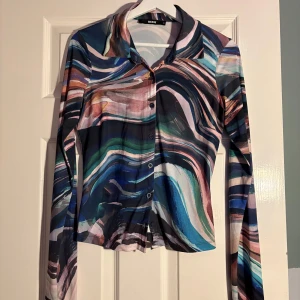 Flerfärgad skjorta från BikBok - Säljer en unik flerfärgad skjorta från BikBok med abstrakt mönster i blått, rosa och grönt. Skjortan har långa ärmar och knappar framtill. Perfekt för dig som vill sticka ut med en färgglad stil!