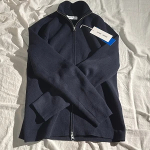 Mörkblå tröja med dragkedja från Samsøe Samsøe - Snygg mörkblå tröja från Samsøe Samsøe med dragkedja och ribbad krage. Perfekt för en stilren look. Tillverkad av återvunnet material. Nypris: 1600kr.  Skick 10/10. Köpte dem för en månad sedan men jag tycker den är lite för liten nu i efterhand. Skriv om minsta funderingar🍾
