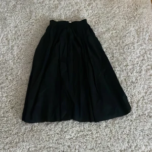 Svart kjol från Arket - Snygg svart kjol från Arket  i en klassisk design. Kjolen har en elastisk midja för extra komfort och en elegant, flödande form som passar perfekt till olika tillfällen. Perfekt för dig som vill ha en stilren look.