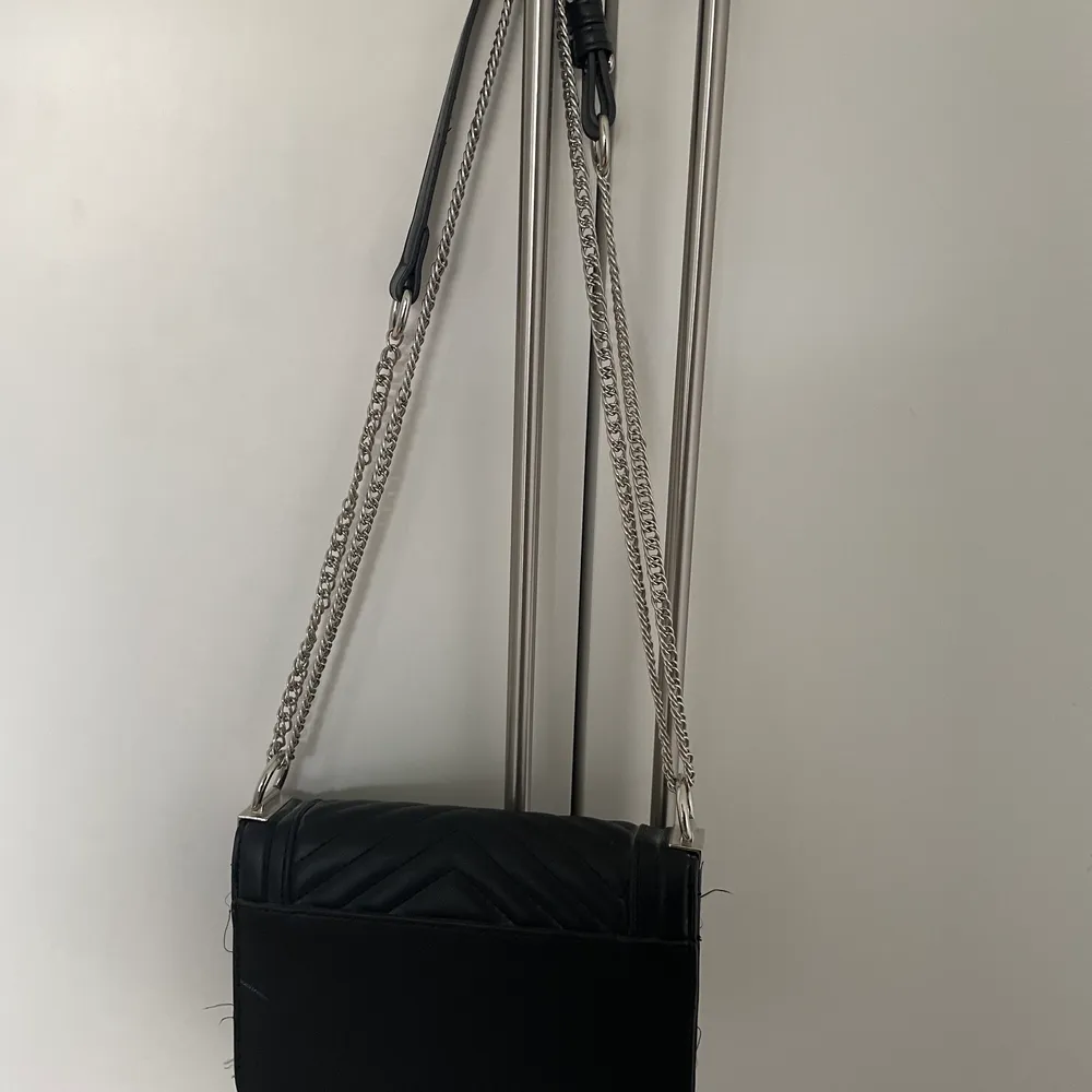 En svart handväska med silver kedja . Väskor.