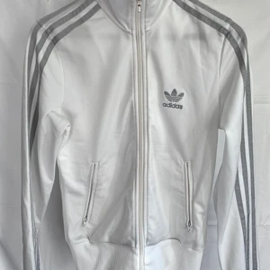 Adidas sweater - Adidas tröja med dragkedja storlek EU34. Vit med silverdetaljer/ märke. Snygg, skön och bra passform. Kan skickas spårbart 66kr!