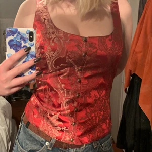 Röd topp  - Jätte fin och originell röd topp. Den sätts på som en väst med knäppning där fram och har ett bad i ryggen som ger superfin passform. Utmärk till fest och sparsamt använd.💋