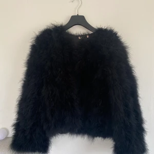 Jacka av äkta strutsfjädrar  - En jättefin svart jacka av strutsfjädrar. Finns knäppning längs med jackan, så den går att stänga om man vill. Storlek vet jag inte. Men passar mig som bär S. Kan fraktas, om köparen står för frakten 🌸✨