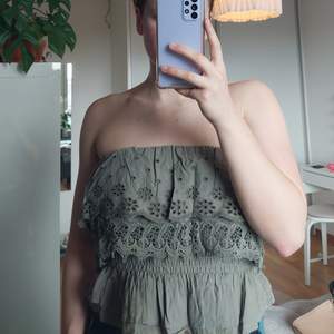 Militärfärgad strapless topp med spetsdetaljer. Den är bara använd ett fåtal gånger så den är i superfint skick😊😊 Storlek S, men är i väldigt stretchigt material så kan även passa större storlekar.